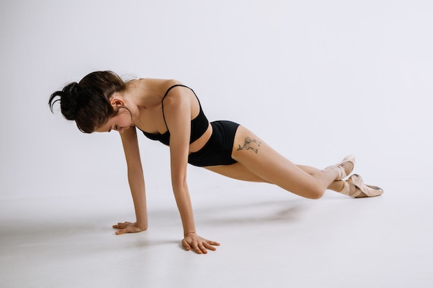 Balé da moda. Jovem bailarina em body preto contra fundo branco. Bailarina caucasiana como um modelo de moda.