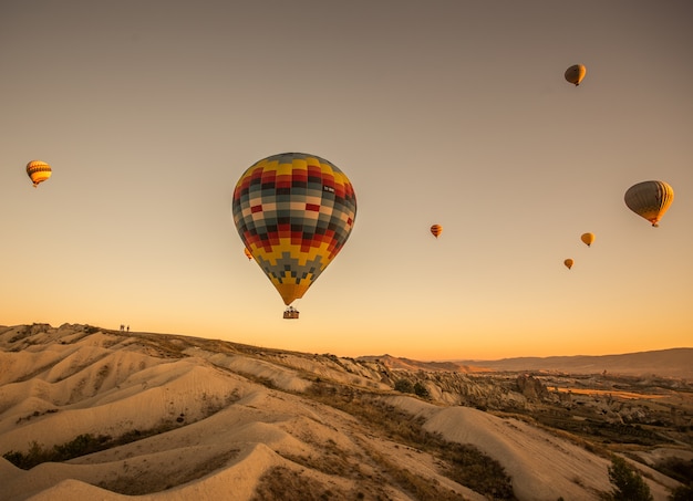 Balões de ar quente sobre as colinas e campos durante o pôr do sol na capadócia, na turquia