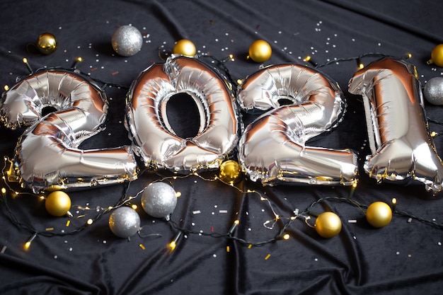 Balões de folha de prata fizeram número de ano novo em fundo preto com guirlanda e bolas.