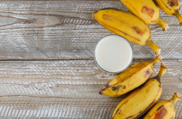 Foto grátis bananas maduras com leite plano deitado sobre uma madeira