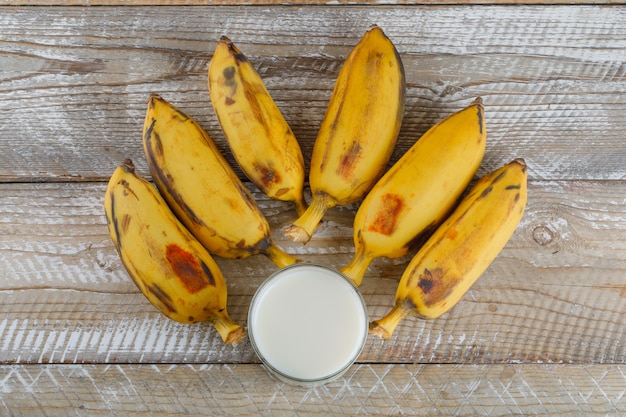 Bananas maduras com leite plano deitado sobre uma madeira