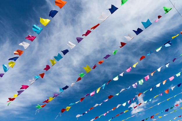 Bandeiras coloridas bonitos pequenas na corda que pendura fora para o feriado com o fundo branco brilhante das nuvens do céu azul. Itália, Sardenha.