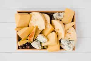 Foto grátis bandeja de madeira com várias fatias do queijo suíço médio-duro com azeitonas verdes