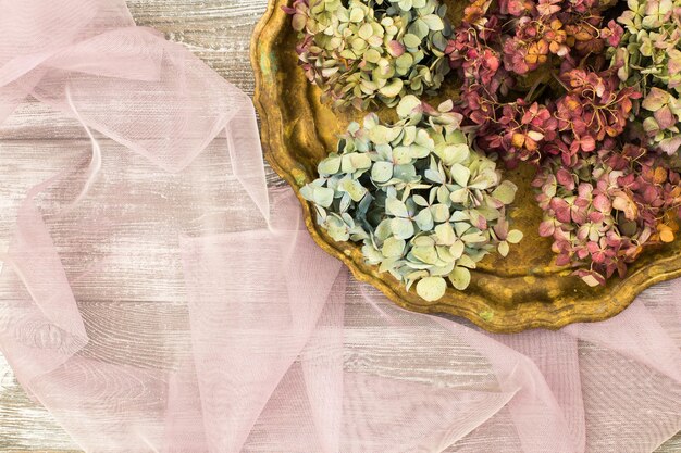 Bandeja vintage com flores secas de hortênsia azul em um tecido de tule transparente roxo em uma mesa cinza. estilo plano. copie o espaço para texto.