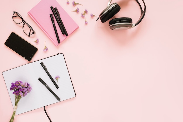 Bando de flores de lavanda; celular; fone de ouvido e artigos de papelaria no fundo rosa