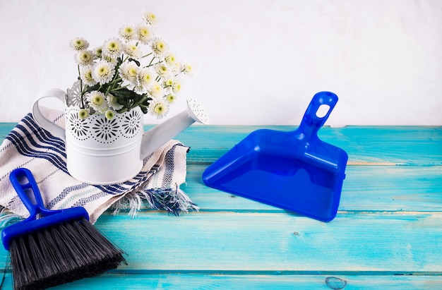 Bando de flores frescas em regador ornamental perto de pincel e dustpan