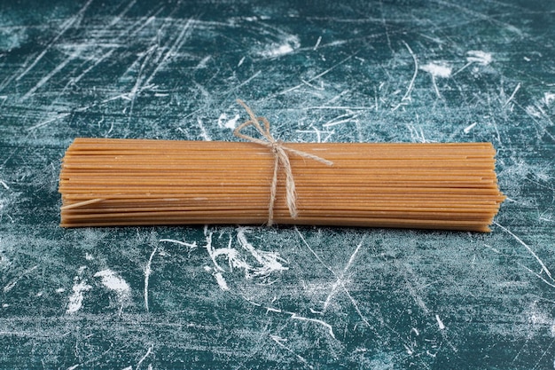 Bando de macarrão de espaguete de grãos inteiros amarrado com corda no espaço de mármore.