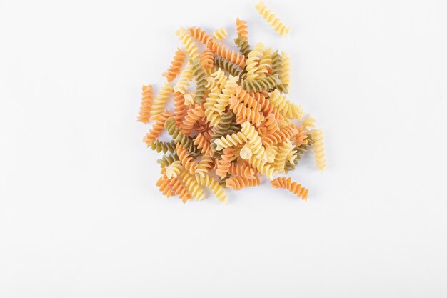 Bando de macarrão fusilli colorido cru na superfície branca.