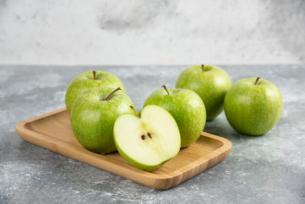 Bando de maçãs verdes inteiras e fatiadas na placa de madeira.