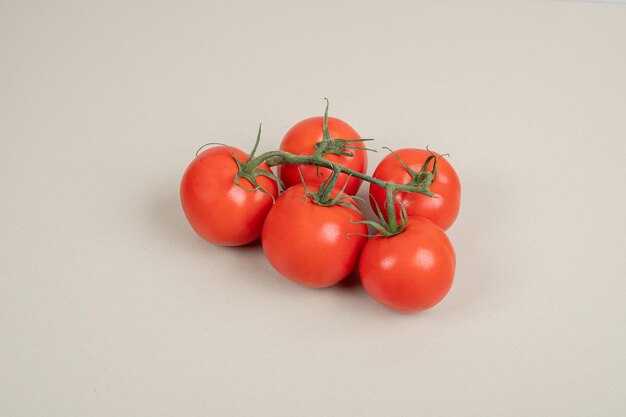 Bando de tomates frescos e vermelhos com hastes verdes na mesa branca.
