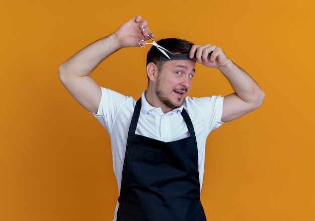 Foto grátis barbeiro de avental penteando e cortando o cabelo em pé sobre fundo laranja