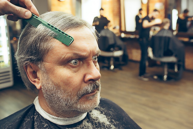 Barbeiro fazendo corte de cabelo atraente velho na barbearia