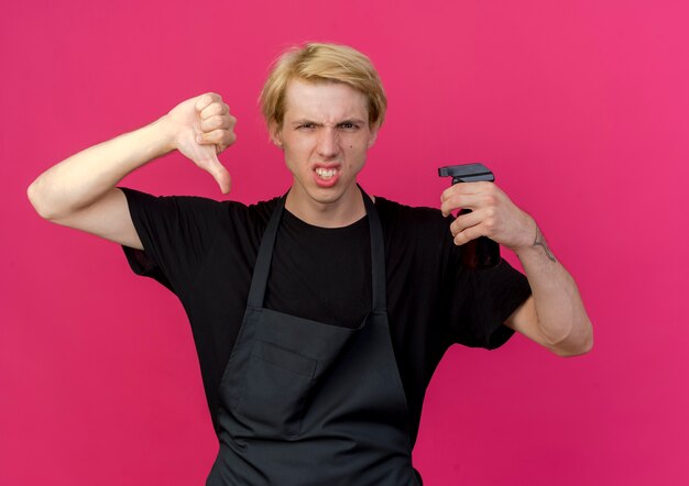 Barbeiro profissional com avental segurando o aparador com cara de raiva mostrando os polegares para baixo