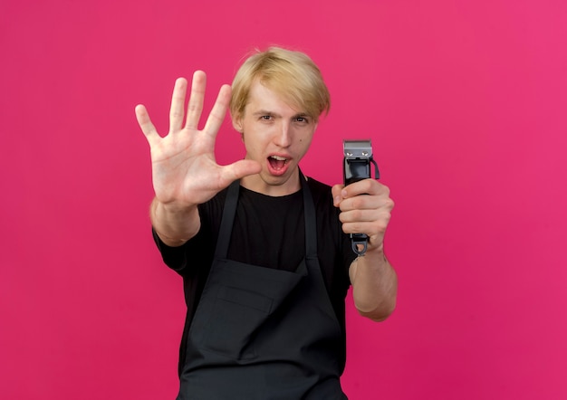 Barbeiro profissional de avental segurando o aparador, mostrando e apontando para cima com os dedos número cinco