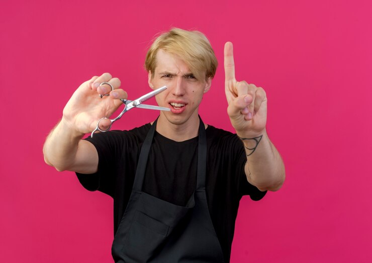 Foto grátis barbeiro profissional de avental segurando uma tesoura, mostrando o dedo indicador com expressão cética em um gesto de advertência