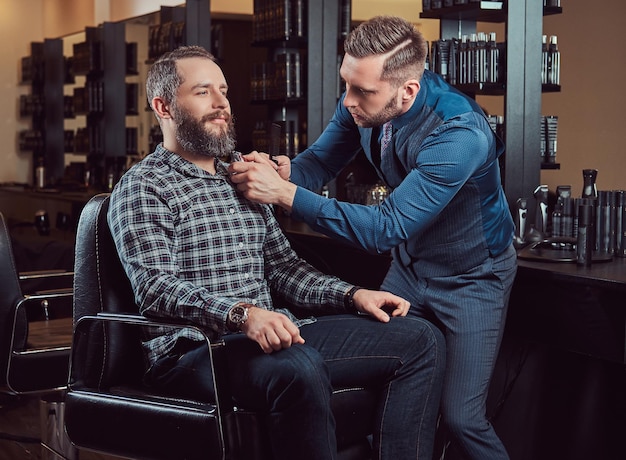 Barbeiro profissional trabalhando com um cliente em um salão de cabeleireiro. Estilizar a barba com um aparador.