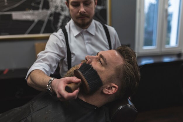 Barbeiro varrendo o cabelo da face do cliente