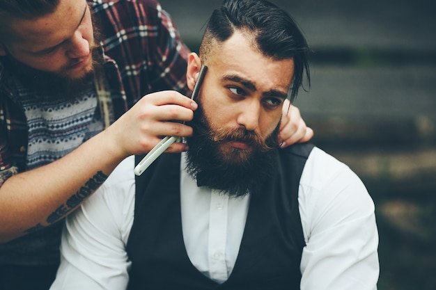 Foto grátis barber faz a barba de um homem barbudo em um ambiente vintage