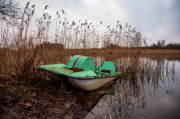 Barco a remo enferrujado abandonado perto do lago em uma área suja