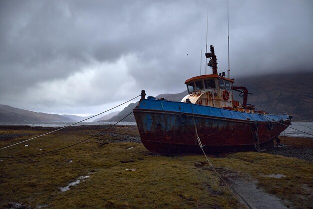 Barco de pesca abandonado encalhado em terra nas terras altas da escócia, reino unido. abandonado, enferrujado e dilapidado. dia de tempestade com muitas nuvens e nevoeiro no ambiente.