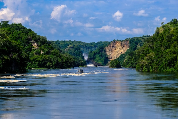 Barco navegando na água no meio de falésias com árvores e plantas com céu azul