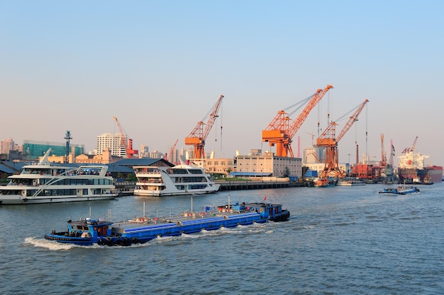 Barco no rio Huangpu com arquitetura urbana de Xangai e guindaste de carga