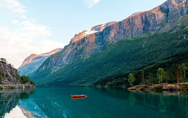 Barco vermelho atracado no lago idílico perto das montanhas rochosas