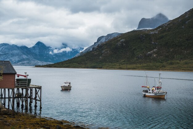 barcos de pesca navegando no lago perto das montanhas sob o céu nublado