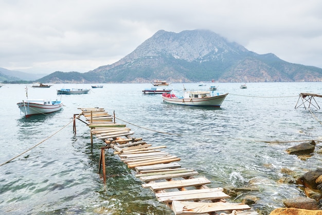 Barcos perto do cais quebrado, colocando em uma água do mar azul tranquila e tranquila.