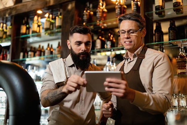 Foto grátis barista adulto médio e seu jovem colega de trabalho usando o touchpad enquanto trabalhava em um pub