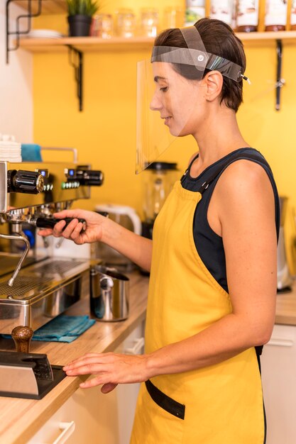 Foto grátis barista de vista lateral no trabalho com proteção facial