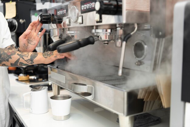 Barista masculino com tatuagens usando a máquina de café da cafeteria