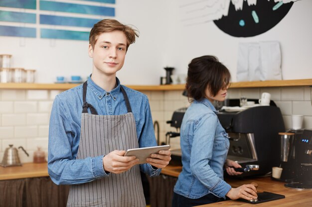 Barista masculino, levando a ordem, segurando a guia, barista feminino fazendo café