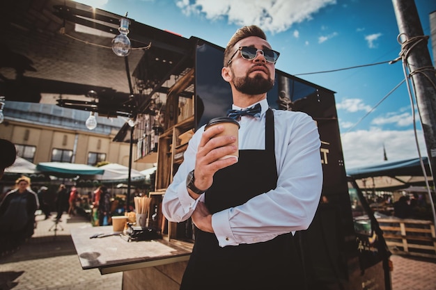 Barista moderno e arrumado em copos tem uma pausa para o café e desfruta de café. há dia de verão ensolarado brilhante.