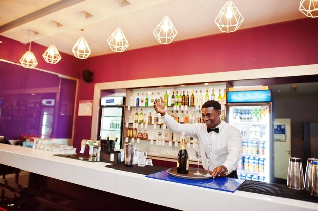Barman americano africano no bar segurando champanhe com copos na bandeja