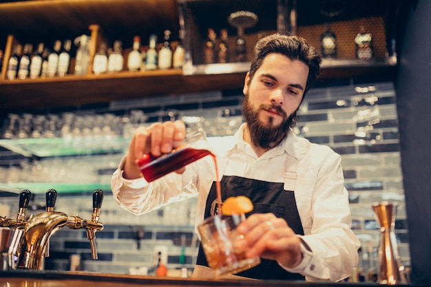 Barman bonito fazendo beber e cocktails num balcão