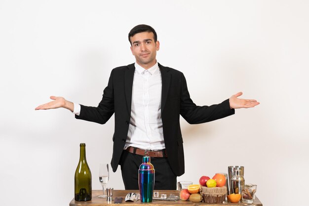 Barman masculino de frente para a mesa com bebidas e coquetéis posando na parede branca bar noturno de bebidas alcoólicas masculinas