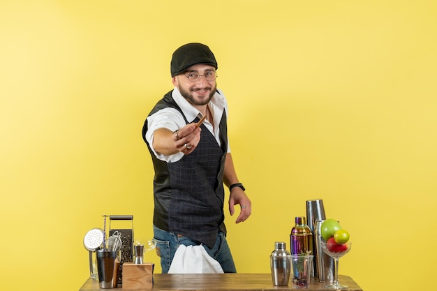 Foto grátis barman masculino de frente para a mesa com shakers sorrindo na parede amarela.