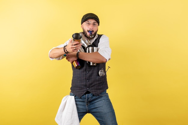 Barman masculino de frente para o bar segurando coquetéis na parede amarela