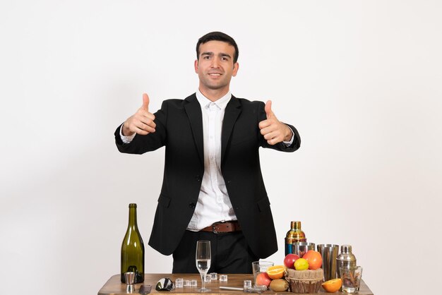 Barman masculino de terno clássico em frente à mesa com bebidas na parede branca bar de bebidas alcoólicas masculinas à noite