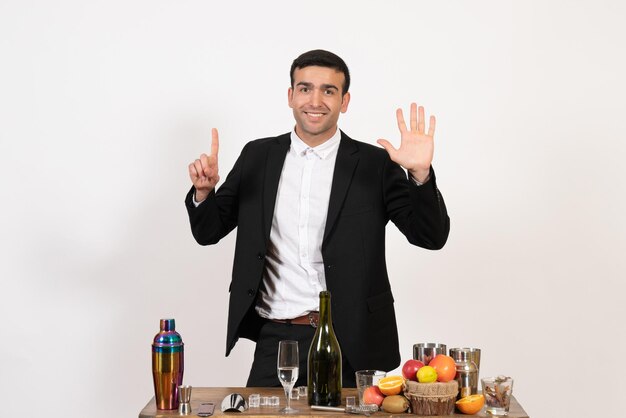 Barman masculino de terno clássico em frente à mesa com bebidas na parede branca clara bar de bebidas alcoólicas noite masculina