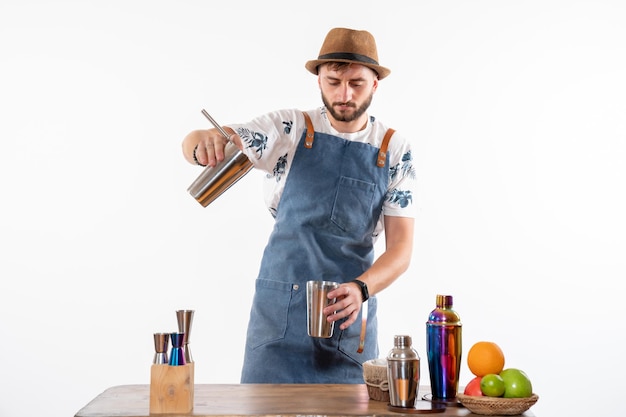 Barman masculino em frente à mesa do bar preparando uma bebida na coqueteleira na parede branca bar álcool trabalho noturno frutas bebida clube