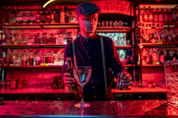 Barman preparando o coquetel alcoólico em luz neon multicolorida, foco no vidro