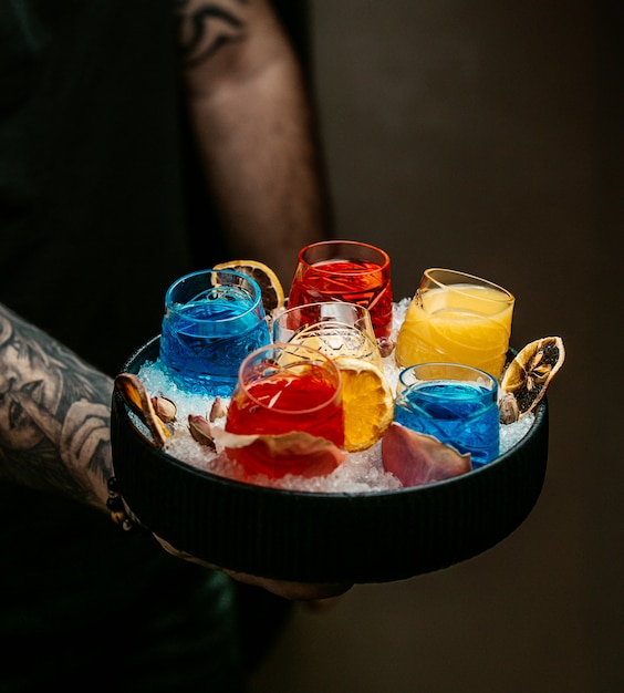 Barman, segurando uma bandeja com cocktails amarelos, azuis e laranja.