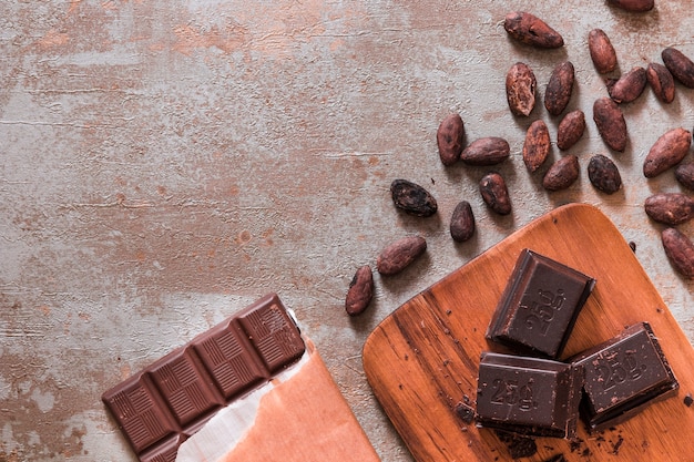 Barra de chocolate e pedaços com grãos de cacau no pano de fundo rústico