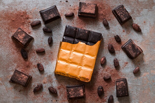 Barra de chocolate embrulhado e grãos de cacau sobre fundo rústico