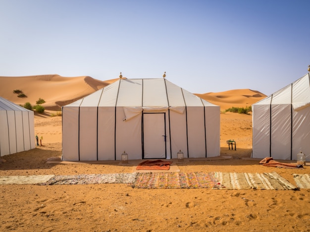 Barracas brancas berberes no deserto do Saara, Marrocos, com tapetes no solo arenoso