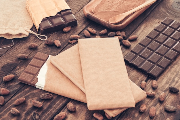 Barras de chocolate escuro com grãos de cacau na mesa de madeira