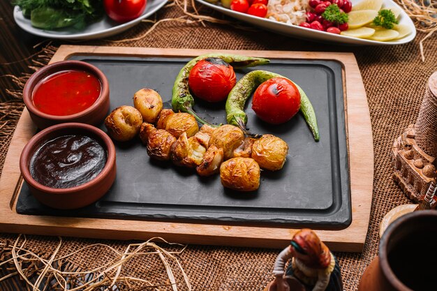 Batata assada na placa de madeira com vista lateral para molhos de tomate pimenta