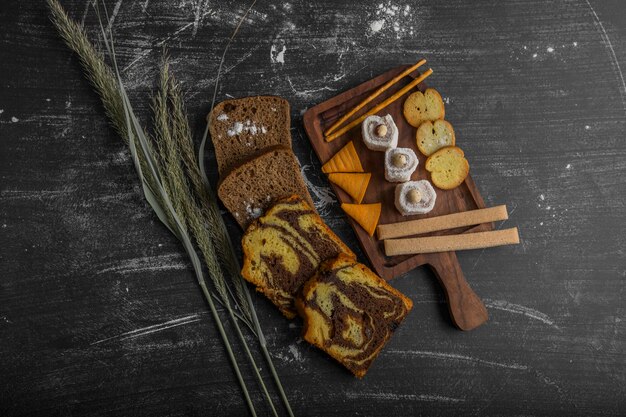 Batata frita com produtos de confeitaria em uma travessa de madeira e fatias de pão à parte, vista de cima